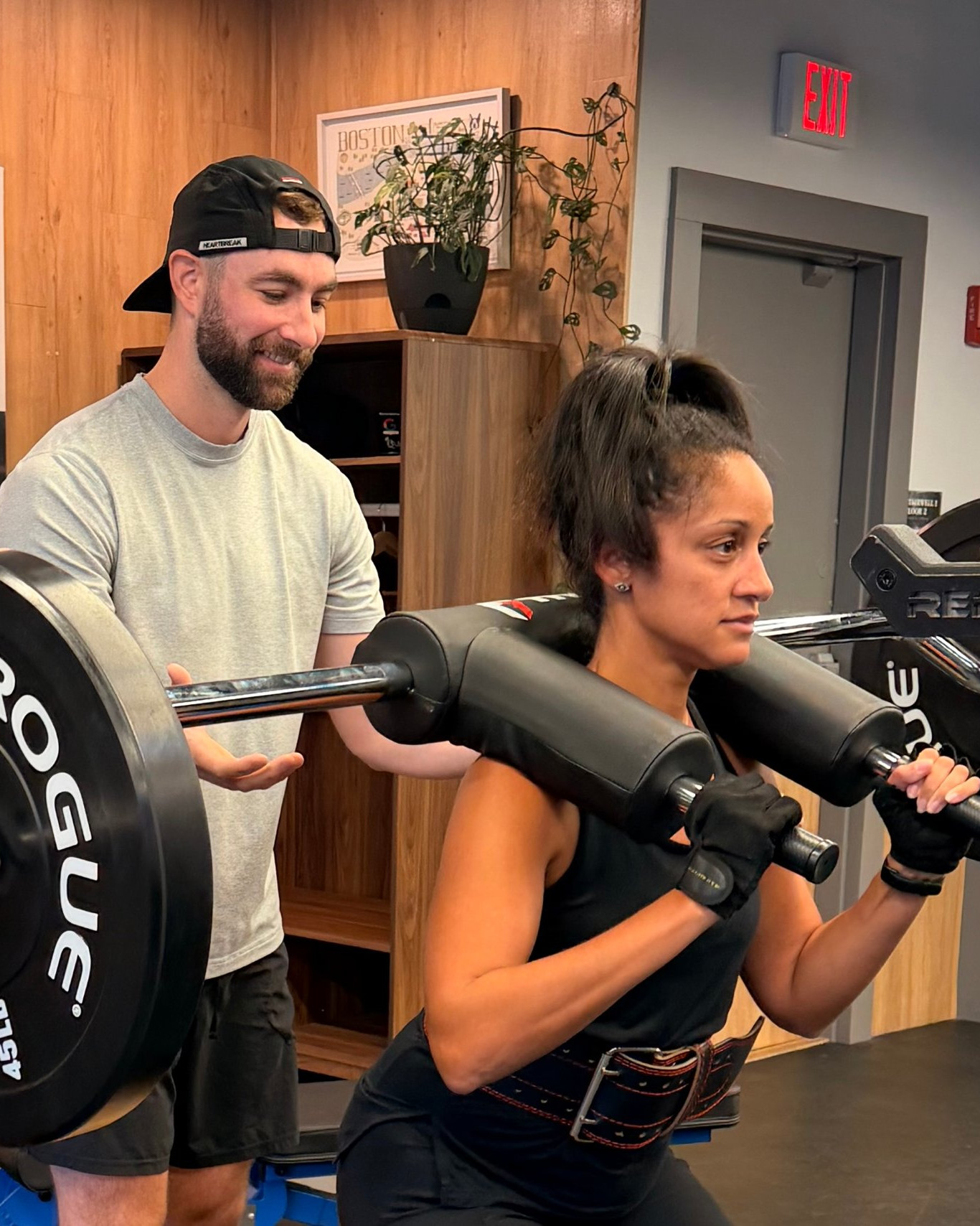 A trainer coaching a client through a safety-bar box squat