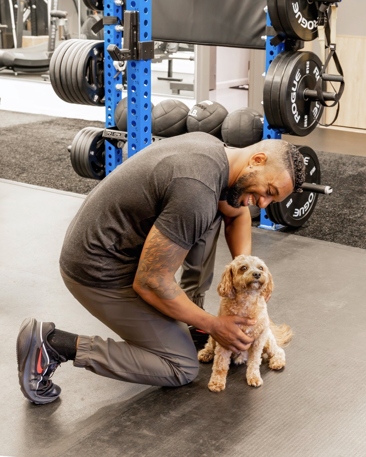 A Studio 617 trainer kneeling on the studio floor to pet a small, fluffy dog