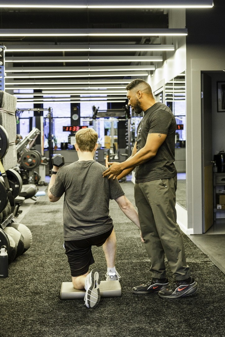 A trainer cueing a client through a half-kneeling dumbbell press on the turf